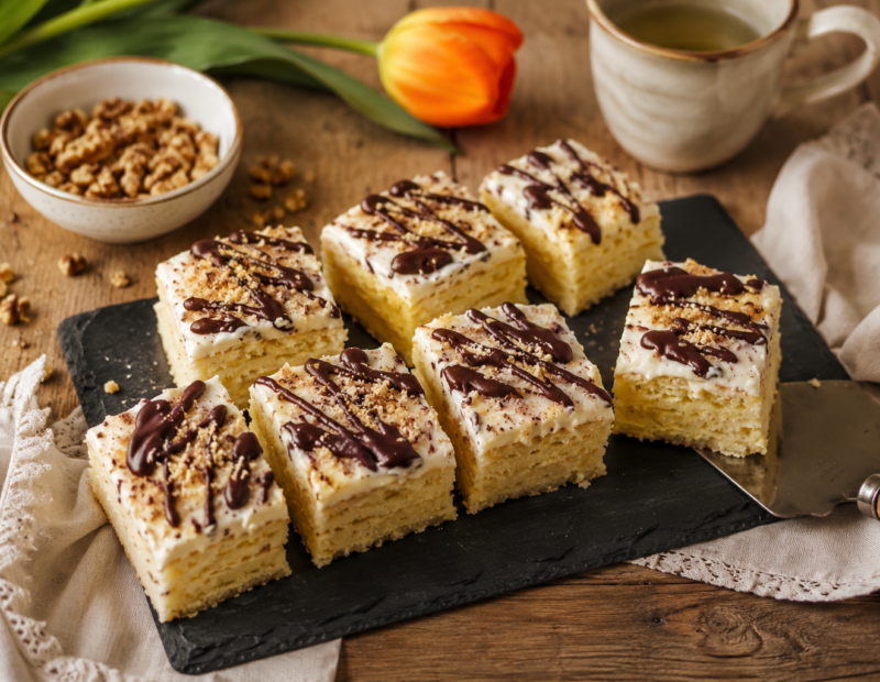 Pineapple cake squares with pale vegan cream, dark chocolate drizzle and walnut crumbs.